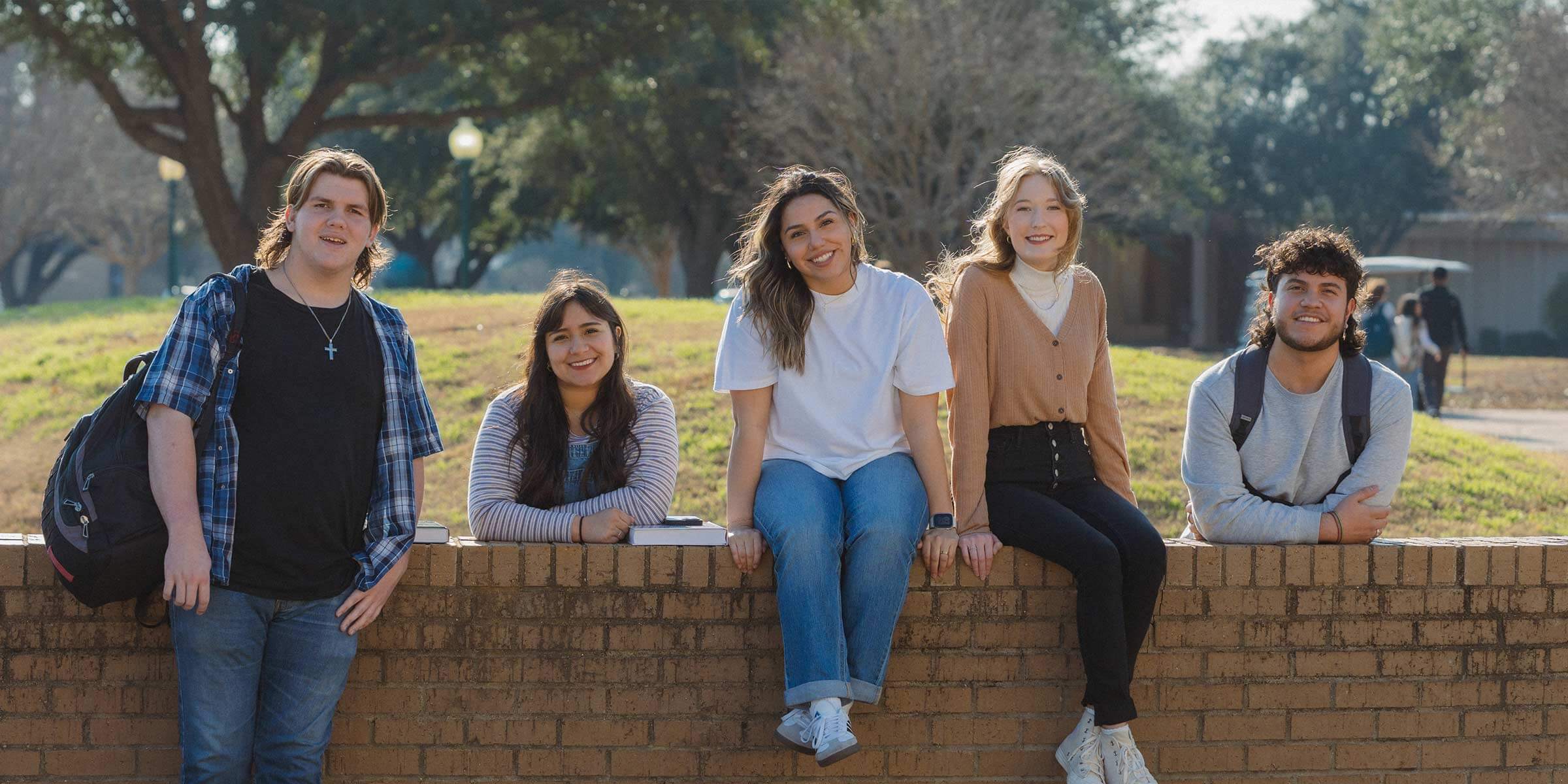 Nelson students near and on brick wall relaxing